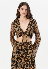 Leopárdminta crop top hosszú ujjal, mély V-nyakkivágással, elülső megkötő részlettel és áttetsző textúrával, párosítva egy hozzá illő szoknyával.