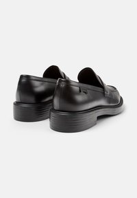 Pair of black leather loafers with chunky stacked heels, visible stitching, and a small branded tag on the outer side of each shoe.