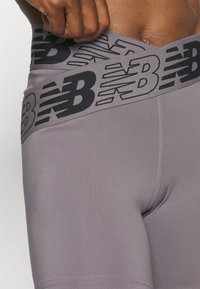 Szare sportowe spodenki z czarną opaską z logo w pasie. Materiał wydaje się gładki i elastyczny, zaprojektowany z myślą o wygodzie podczas aktywności.