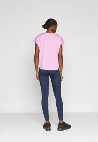 Ανοιχτό ροζ τοπ με κοντά μανίκια και άνετη εφαρμογή, σε συνδυασμό με ναυτικό κολάν με διακριτικές ριγέ λεπτομέρειες. Μαύρα αθλητικά παπούτσια συμπληρώνουν το σύνολο.