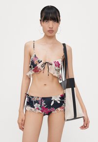 Blomstrete to-delt bikini med volanger i marineblått og krem; har justerbare bånd, sammen med en svart og kremtote bag.