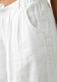 Białe lniane szorty z elastycznym paskiem w talii, bocznymi kieszeniami i lekko teksturowaną powierzchnią, charakteryzujące się luźnym krojem odpowiednim do codziennego noszenia.