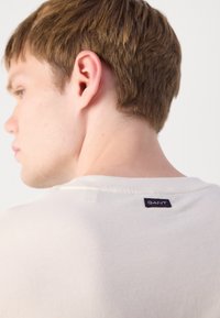 Light beige t-shirt with a round neckline. It features a small GANT label at the back neck and a smooth, soft texture.
