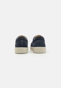 Navy suede slip-on shoes with a beige rubber sole, featuring a minimalist design and seamless upper with subtle branding on the heel.