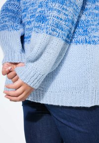 Jasnoniebieski sweter dziany w różnych odcieniach niebieskiego, z ściągaczami na rękawach i luźnym krojem, wykonany z miękkiej, teksturowanej przędzy.