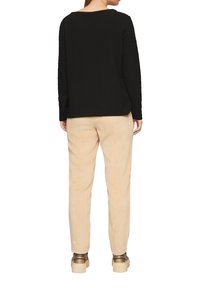 Haut à manches longues texturé noir associé à un pantalon en velours côtelé beige. Des chaussures à plateforme marron complètent la tenue. Vue de l'arrière.
