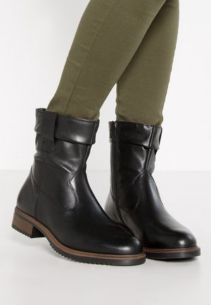 Bottines en cuir noir avec un revers, fermeture éclair latérale et un petit talon empilé. Surface texturée avec une finition lisse et un accent en bois.