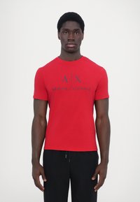 Raudona trumparankovė medvilninė T-palaidinė su apvalia iškirpte ir dideliu juodu "A|X ARMANI EXCHANGE" logotipo spaudiniu priekyje.