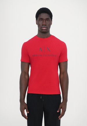 T-shirt en coton rouge à manches courtes avec un col rond et un grand logo noir "A|X ARMANI EXCHANGE" imprimé sur le devant.