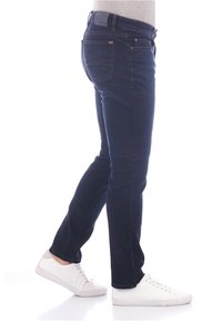 Jeans de mezclilla azul oscuro con un ajuste slim, con bolsillos traseros y detalles de costura clara, combinados con zapatillas blancas.