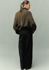 Suéter de punto verde oliva de gran tamaño con cuello vuelto, combinado con pantalones de pierna ancha negros de cintura alta. Textura suave, detalles mínimos.