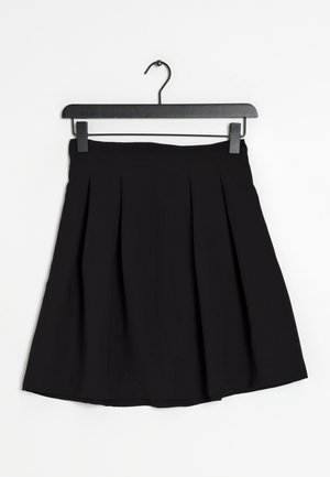 Falda negra plisada hasta la rodilla colgada en una percha negra sobre un fondo blanco.