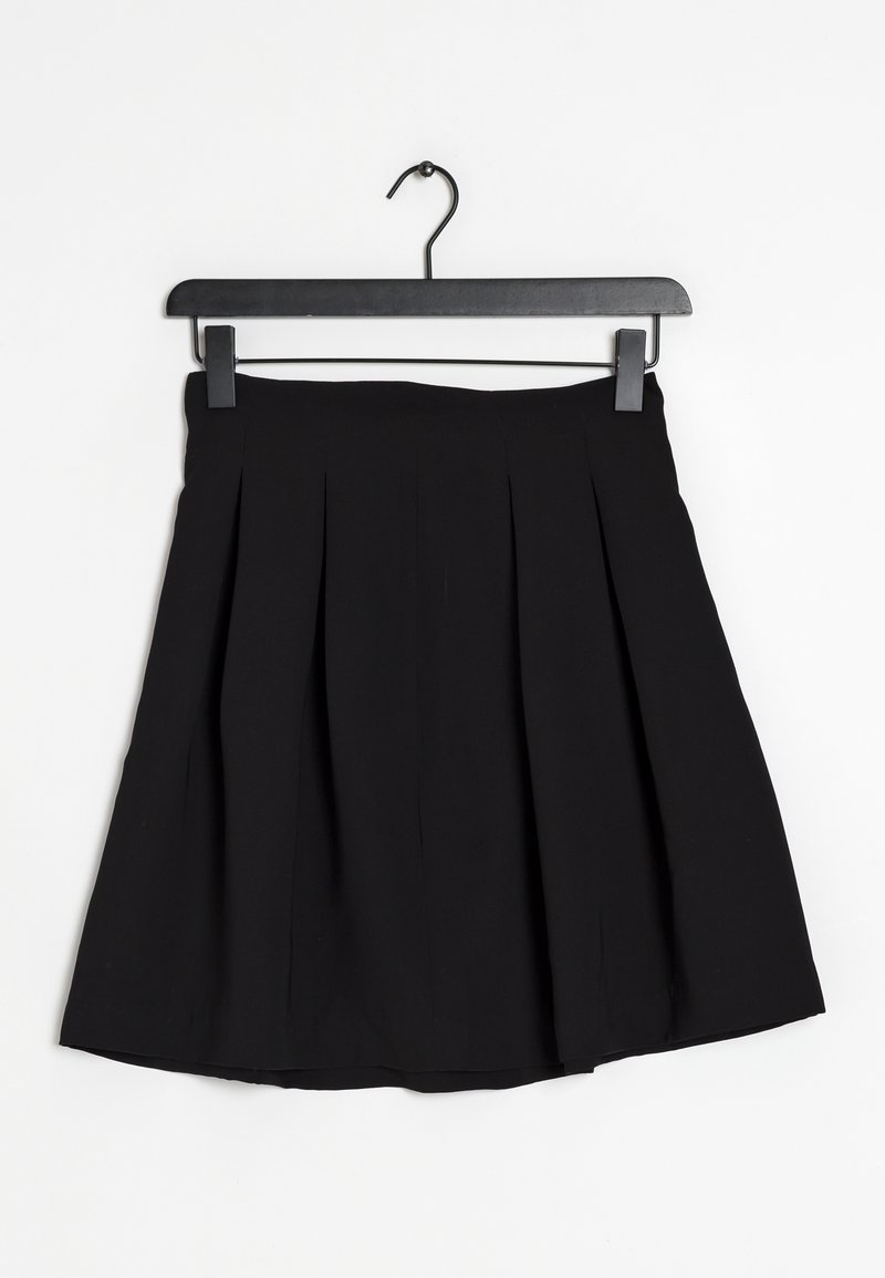 Jupe plissée noire longueur genou accrochée à un cintre noir sur un fond blanc.