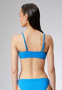 Blauer, gerippter Bikini-Oberteil und -Unterteil mit dünnen, verstellbaren Trägern. Verfügt über ein nahtloses Design und eine strukturierte Oberfläche. Keine sichtbaren Verzierungen.