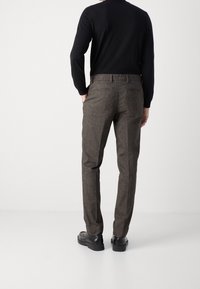 Brązowe spodnie z mieszanki wełny o teksturowanym wykończeniu, slim fit, z bocznymi kieszeniami. Z tyłu znajdują się dwie kieszenie. Noszone z czarną bluzką z długim rękawem.