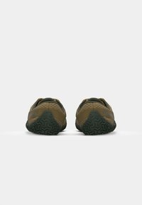 Zapatillas deportivas verdes y marrones con patrones texturizados, una suela flexible y talón reforzado. El diseño incluye un sutil detalle de marca.