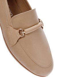 Mocassino in pelle beige con dettaglio in metallo dorato e cuciture decorative. La punta arrotondata e la texture liscia arricchiscono il design.