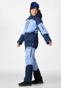 Skianzug in Blau und Hellblau, mit Kapuze, mehreren Reißverschluss-Taschen und verstellbaren Manschetten. Aus robustem Stoff und mit Isolation versehen.