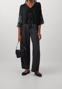 Haut court noir avec manches cloche bordées de dentelle, devant avec cordon de serrage. Pantalon gris à jambes larges, ballerines noires et petit sac à main noir.