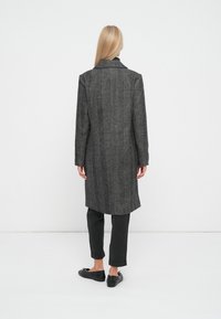 Cappotto in lana a spina di pesce grigio con un design lungo e dritto, collo a revers e una vestibilità sartoriale, abbinato a pantaloni scuri e scarpe nere.