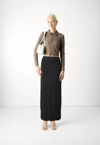 Hnedý rebrovaný dlhý rukáv polo crop top skombinovaný s čiernou dlhou sukňou a tenkými priehľadnými podpätkami, doplnený malou bielou kabelkou.