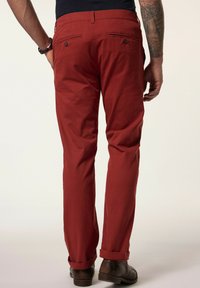 Pantaloni in cotone rossi con taglio dritto, dotati di due tasche posteriori e orlo arricciato, abbinati a scarpe in pelle marrone.