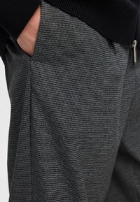 Grau gemusterte Stoffhosen mit strukturierter Webart, seitlichen Taschen und einem lässigen Schnitt. Akzentuiert durch einen schwarzen Bund.