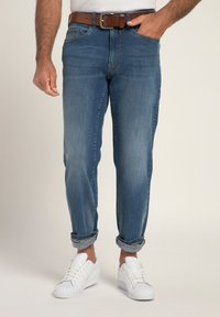 Vaqueros de denim en azul con un corte relajado, puños doblados y diseño de cinco bolsillos. Combinados con un cinturón marrón y zapatillas blancas.