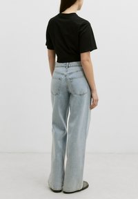 Hoge taille lichtblauwe denim jeans met een relaxte pasvorm en zichtbare achterzakken, gecombineerd met een getailleerd zwart T-shirt.