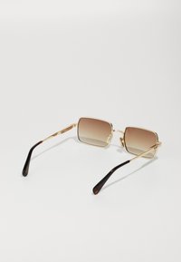 Lunettes de soleil en métal doré avec des montures carrées, des verres brun dégradé et des accents en écaille sombre sur les branches. Texture lisse sur l'ensemble.