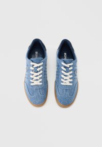 Dżinsowe trampki z białymi sznurowadłami, beżowymi gumowymi podeszwami i perforowanym wzorem, posiadające zaokrąglony nosek i gładką teksturę.