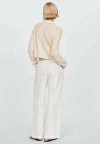 Jasnoróżowy sweter w robótki z cropped designem, zestawiony z białymi spodniami o szerokich nogawkach, charakteryzującymi się gładką teksturą i minimalnymi detalami.