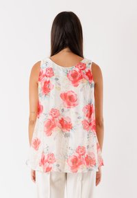 Blusa senza maniche floreale con uno sfondo chiaro e grandi rose rosse, dettagli verdi, scollatura arrotondata e un design fluido e leggero.