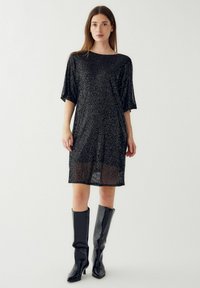 Rochie neagră cu paiete, cu o croială lejeră, mâneci scurte și lungime până la genunchi. Asortată cu cizme negre din piele lacuită, până la genunchi.