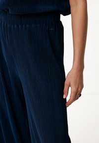 Marinblå rynkade byxor med elastisk midja; mjuk textur; har en liten logotypetikett vid midjan; avslappnad passform.