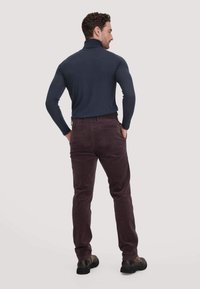 Donkerblauwe coltrui gecombineerd met bordeaux kleurige corduroy broek. Model staat met de rug naar de camera, waarbij het aansluitende ontwerp en de details van de textuur goed zichtbaar zijn.
