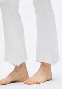 Pantalon blanc en coton léger avec une coupe décontractée, présentant un ourlet irrégulier et des bords bruts. Conçu pour le confort et la liberté de mouvement.