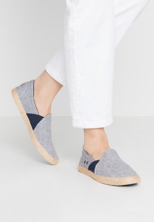 Chaussures slip-on en toile avec un schéma de couleurs gris et bleu marine, une semelle en jute de style espadrille, et une tige texturée avec un design superposé.