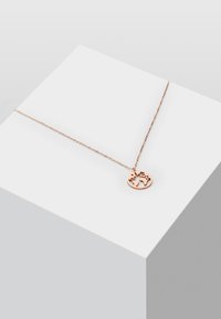 Collana in oro rosa con un pendente circolare che presenta un design della mappa del mondo, appesa a una delicata catena, esposta su un piedistallo geometrico.