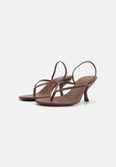 Sandalias de tacón marrones con un diseño minimalista que presenta una delgada tira en el dedo del pie y correas delgadas en el tobillo. Textura suave y forma de tacón curvada.