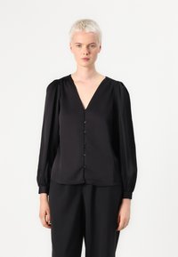 Blusa negra con escote en V, mangas largas abullonadas y botonera en la parte delantera. Textura de tela suave, corte holgado.