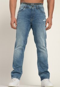 Jeans de mezclilla azul claro con un corte recto, que presentan sutiles detalles desgastados, costuras en contraste y una cinturilla elástica marcada con "STHUGE".