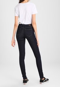 Smala mörka denimjeans med hög midja och subtila sömmar, i kombination med en enkel vit t-shirt och svarta sneakers.