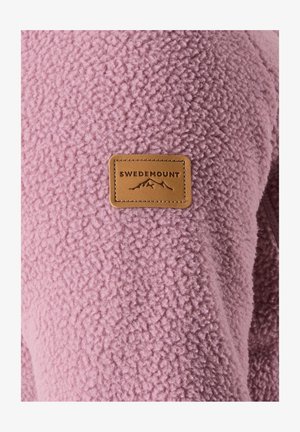 Fleece-takki vaaleanpunaisena, jossa on teksturoitu pinta. Varustettu ruskealla nahkalapulla, jossa on teksti "SWDEMOUNT" ja vuoristokuvio.