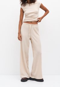 Beżowy zestaw z miękkim prążkowanym splotem, obejmujący krótki top z okrągłym dekoltem oraz wysokiej talii szerokie spodnie z paskiem na sznurki.