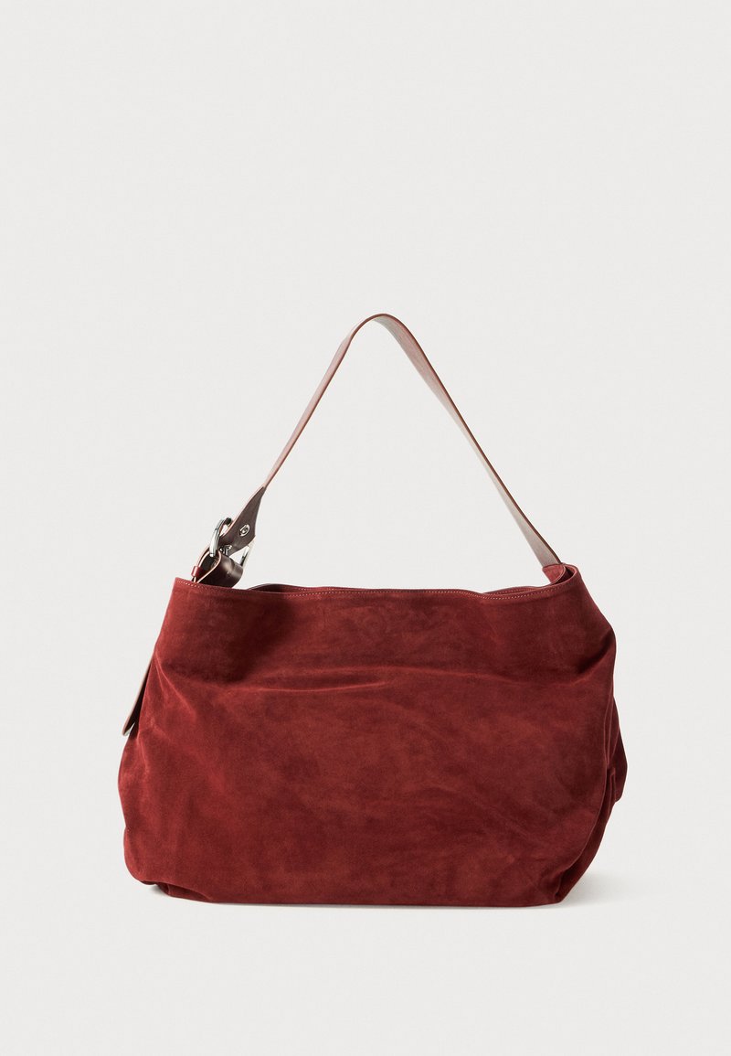Sac à épaule en suède rouge doux avec une seule bandoulière en cuir beige clair et des éléments en métal argenté sur fond blanc.