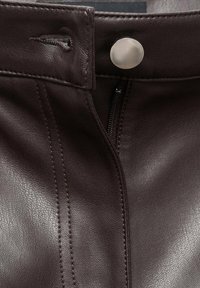 Brown leather skirt featuring a front zipper and snap closure, with vertical seams and a textured finish. Metal hardware visible.