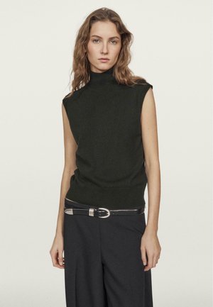 Schwarzer ärmelloser Rollkragenpullover aus weicher Stoff, kombiniert mit hoch taillierten schwarzen Hosen und einem silbernen Gürtelakzent.