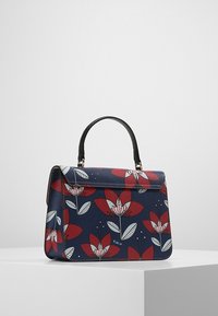 Námořnická kabelka s květinovým vzorem v červené a bílé. Má strukturovaný design, černou rukojeť a magnetické uzavření na klopě. Texturovaný povrch.