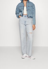 Světle modrá džínová bunda s kapucí, krátký střih a elastické manžety, doplněná o světle modré džíny s vysokým pasem a efektem ošoupání.